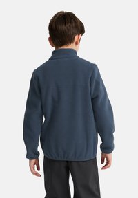 Giacca in pile blu scuro con alta collana e maniche lunghe, caratterizzata da una superficie liscia e orlo elastico, vista da dietro.