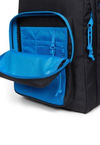 Mochila negra con un compartimento con cremallera de tela azul y un bolsillo de malla, con una superficie suave, destacando colores contrastantes y un diseño funcional.
