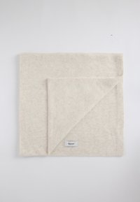 Couverture en laine beige clair, présentant une texture douce et un bord replié dévoilant une face inférieure légèrement plus foncée. Étiquette visible dans le coin inférieur.