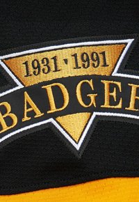 Schwarzes und goldenes besticktes Abzeichen mit "BISAMRATTE" und einem dreieckigen Design sowie den Jahren "1931-1991" in fettem Text auf strukturiertem Stoff.