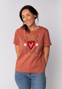 Weiche terrakottafarbene T-Shirt mit kurzen Ärmeln, das ein Herz- und Blumendesign in roten, rosafarbenen und goldenen Tönen zeigt; runder Halsausschnitt; lässige Passform.