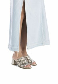 Sandali con tacco a blocco intrecciati nei toni metallici d'oro e argento, design open-toe, abbinati a una lunga gonna in denim chiaro con spacco laterale.