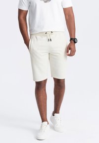 Cremefarvede shorts lavet af blødt stof, med en elastisk talje og snor, sidelommer og en afslappet pasform.