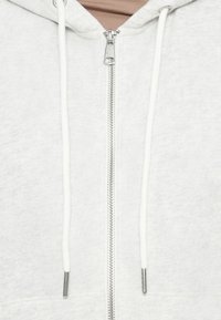 Felpa grigia chiara con zip in tessuto morbido. Presenta una zip argentata, lacci e tasche frontali. Design semplice con vestibilità comoda.