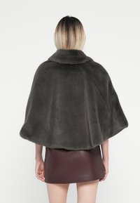 Graue Kunstfell-Cape mit hohem Kragen, weicher Textur, abgerundeten Kanten und offenem Design. Kombiniert mit einem figurnahen burgunderfarbenen Minirock.