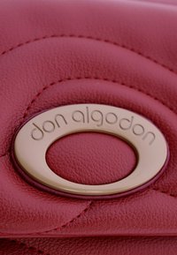 Bolso de cuero rojo con textura, herrajes ovalados en tono dorado con el nombre de la marca grabado, costuras decorativas y un diseño acolchado curvo.