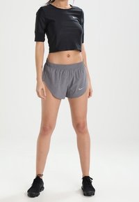 Svart kortärmad idrottströja med korta ärmar och ett par grå lätta löparshorts med geometriskt mönster, bärs med svarta sneakers.