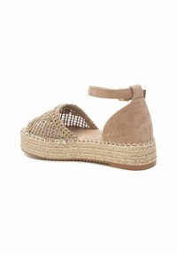 Sandalía de ante color marrón claro con tira al tobillo, parte superior de tejido trenzado, plataforma de yute estilo espadrille y costura decorativa a lo largo de la suela.