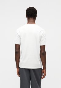 Λευκό βαμβακερό t-shirt με στρογγυλή λαιμόκοψη και κοντά μανίκια, με απλή πίσω όψη και διακριτικό πλαϊνό λογότυπο. Ομαλή υφή, κανονική εφαρμογή.