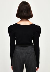 Czarny prążkowany top z bufkami na rękawach i szerokim dekoltem, zestawiony z szarymi spodniami w prążki z tylną kieszenią.
