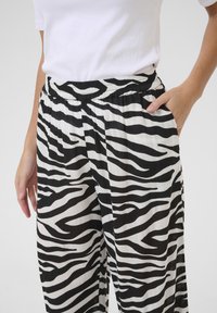 Fekete-fehér zebra mintás nadrág széles lábakkal, redőzött textúrával és rugalmas derékrésszel, oldalsó zsebekkel.