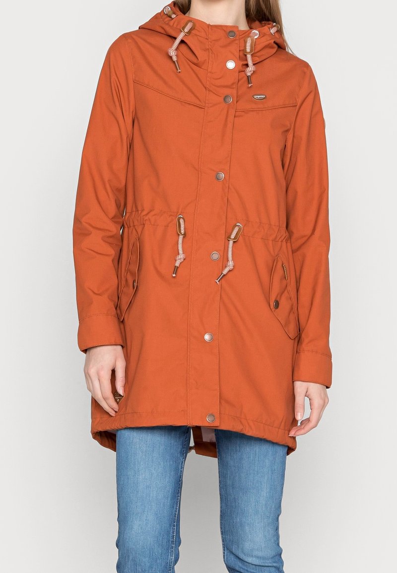 Pomarańczowy wodoodporny parka z kapturem na sznurku, z zapięciem na napy, dwoma bocznymi kieszeniami i regulowanym pasem, wykonany z gładkiego, lekkiego materiału.