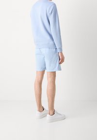 Felpa azzurra chiara e pantaloni corti abbinati. La felpa ha un collo rotondo e maniche lunghe. Sneakers bianche completano l'outfit.