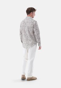 Men's long-sleeve shirt in a light paisley print, featuring a collared neck and soft fabric. Paired with white trousers and beige boots.
