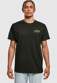 Tricou negru din bumbac cu un imprimeu mic verde și alb pe piept care spune "Los Angeles COMPTON din 1987." Design clasic cu guler round.