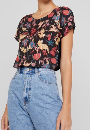 Sort kortærmet top med et blomstermønster i rød, blå og gul. Løs pasform med rund halsudskæring, parret med højtaljede blå jeans.