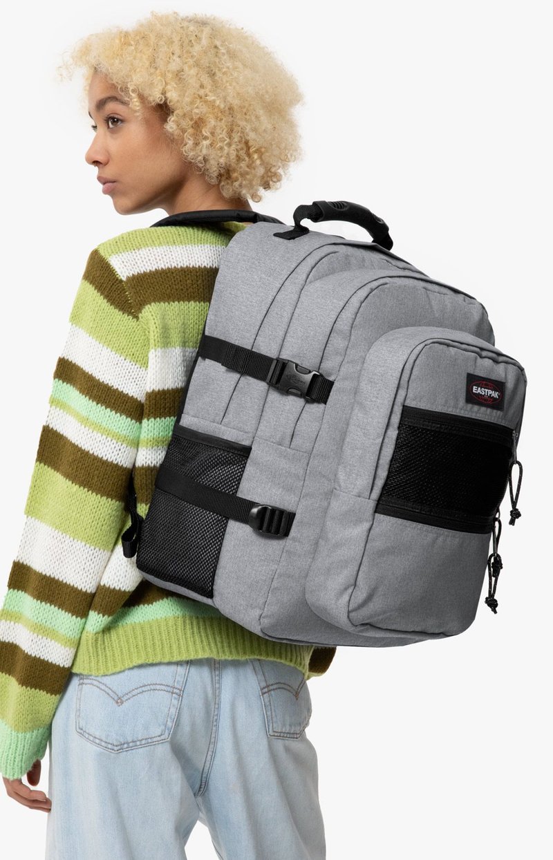 Mochila gris con múltiples compartimentos, acentos negros y correas ajustables. Tejido texturizado con un diseño estructurado.