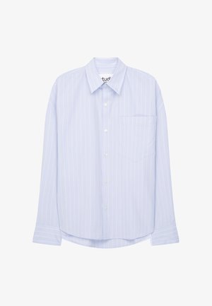 Helles blau gestreiftes Hemd mit spitzen Kragen, langen Ärmeln und einer Brusttasche, kombiniert mit locker sitzenden marineblauen Hosen und weißen Sneakers.