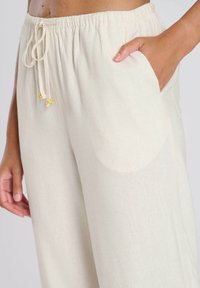 Pantalons larges en mélange de lin de couleur beige crémeux, dotés d'une taille élastique, d'un cordon de serrage avec des accents d'étoiles dorées et de poches latérales.