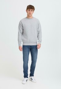 Hallhalli hall sweatshirt ribadega varrukatele, koos tumedate siniste kitsaste teksade ja valgete tennisetega mustade triipudega.
