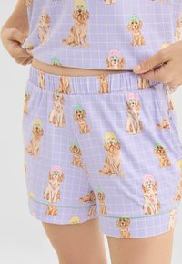 Lavendelkleurige pyjama met een rasterpatroon met herhalende illustraties van honden die kleurrijke hoeden en zonnebrillen dragen. Elastische tailleband, lichtgewicht materiaal.