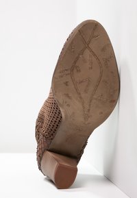 Zapato marrón perforado con una superficie texturizada, tacón bajo en bloque y una suela estampada con detalles en relieve y marca.
