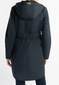 Tmavě modrý dlouhý kabát se stahovacím pasem a kapucí, vyrobený z hladkého, voděodolného materiálu. Má nastavitelné manžety a zadní štítkovou značku.