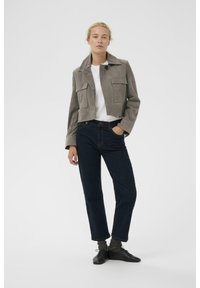 Apkirptas pilkos spalvos zomšinė striukė su dviem krūtinės kišenėmis, derinama su tamsiai mėlynomis tiesiomis džinsų kelnėmis ir juodais bateliais su raišteliais. Po apačia - balti marškinėliai.