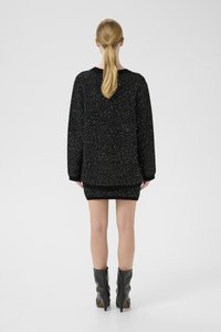 Žena s blond copom, oblečená v čierno-bielom textúrovanom dlhom svetre a zodpovedajúcej krátkej sukni, doplnená čiernymi čižmami s opätkom po lýtka.