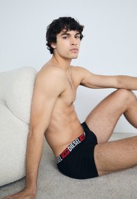 Black boxer briefs with a wide white and red branded waistband. The fabric appears smooth and elastic, fitting snugly on the body.