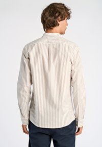 Camicia da uomo a maniche lunghe di un beige chiaro con strisce verticali bianche. Caratterizzata da un colletto con bottoni e orlo arrotondato, in tessuto morbido e testurizzato.