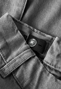 Uma vista de perto do botão ajustável e da faixa elástica dentro da cintura de calças de denim cinza para ajuste de tamanho.