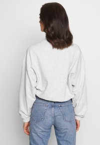 Sudadera de gran tamaño en gris claro con costuras de hombro caídas, puños acanalados y escote en la espalda. Combinada con jeans azules que tienen bolsillos traseros.