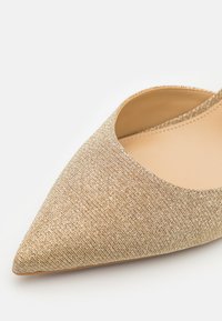 Gold textured pointy-toed flat with an open upper design and smooth beige insole, featuring a sleek and minimalist silhouette.