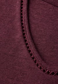 Top de punto burdeos con escote redondo, que presenta un acabado de ganchillo a lo largo del borde, textura suave y vista en primer plano de los detalles de la tela.