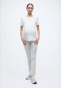 Valge lühikeste varrukatega pluus, helehallid tekstuuriga püksid ja heledad tossud. Vabaaja rõivastus mugavuseks, mis esitleb lõdvestunud istuvust.