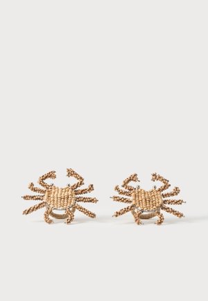 Deux bagues en forme de crabe faites de petites perles beige avec des accents argentés sur un fond clair uni.
