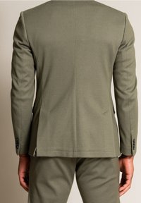 Blazer su misura verde oliva con tessuto testurizzato, revers a punta e due spacchi posteriori. Presenta bottoni neri sulle maniche.