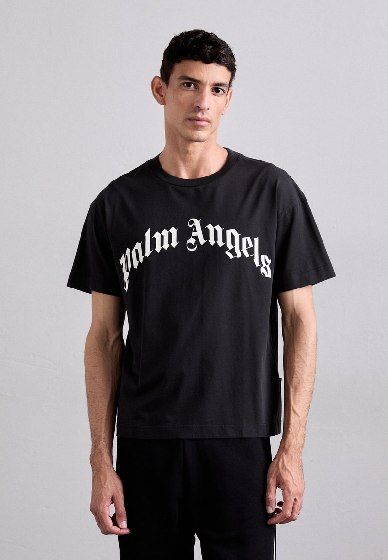 Melnas kokvilnas t-krekls ar "Palm Angels" logo baltā krāsā, ar brīvu piegriezumu un apaļu kakla izgriezumu. Gluda tekstūra un īsās piedurknes.