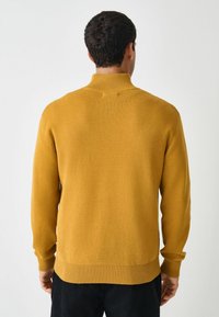 Maglione a maglia giallo senape con colletto alto e polsini a coste. Tessuto morbido e vestibilità rilassata. Orlo sagomato. Vista posteriore.