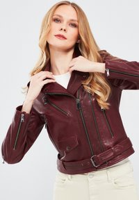 Bordeaux leren bikerjack met zilveren ritsen, meerdere ritszakken en een riem in de taille. Heeft een gekarteld kraag en een strakke pasvorm.