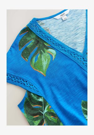 Haut en tissu bleu avec un imprime de feuilles vertes, présentant un col en V et une bordure en dentelle au niveau du col et des manches. Texture douce, design décontracté.