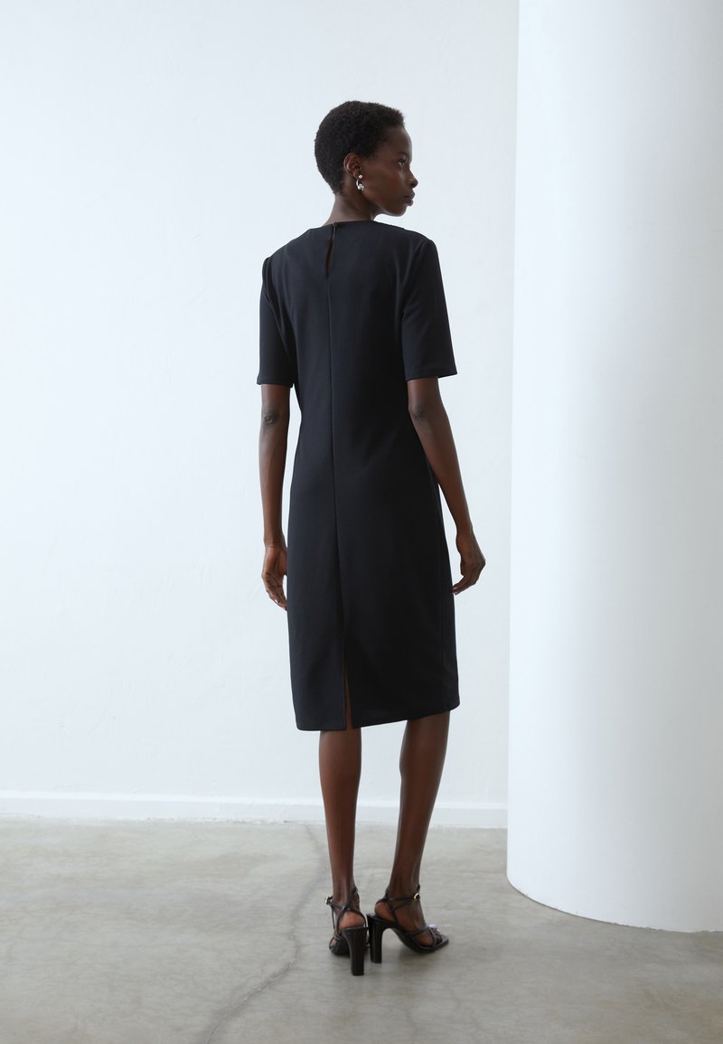 Schwarzes knielanges Kleid mit kurzen Ärmeln, Rückenschlitzdetails und hohem Kragen. Glattes Material und minimalistisches Design.