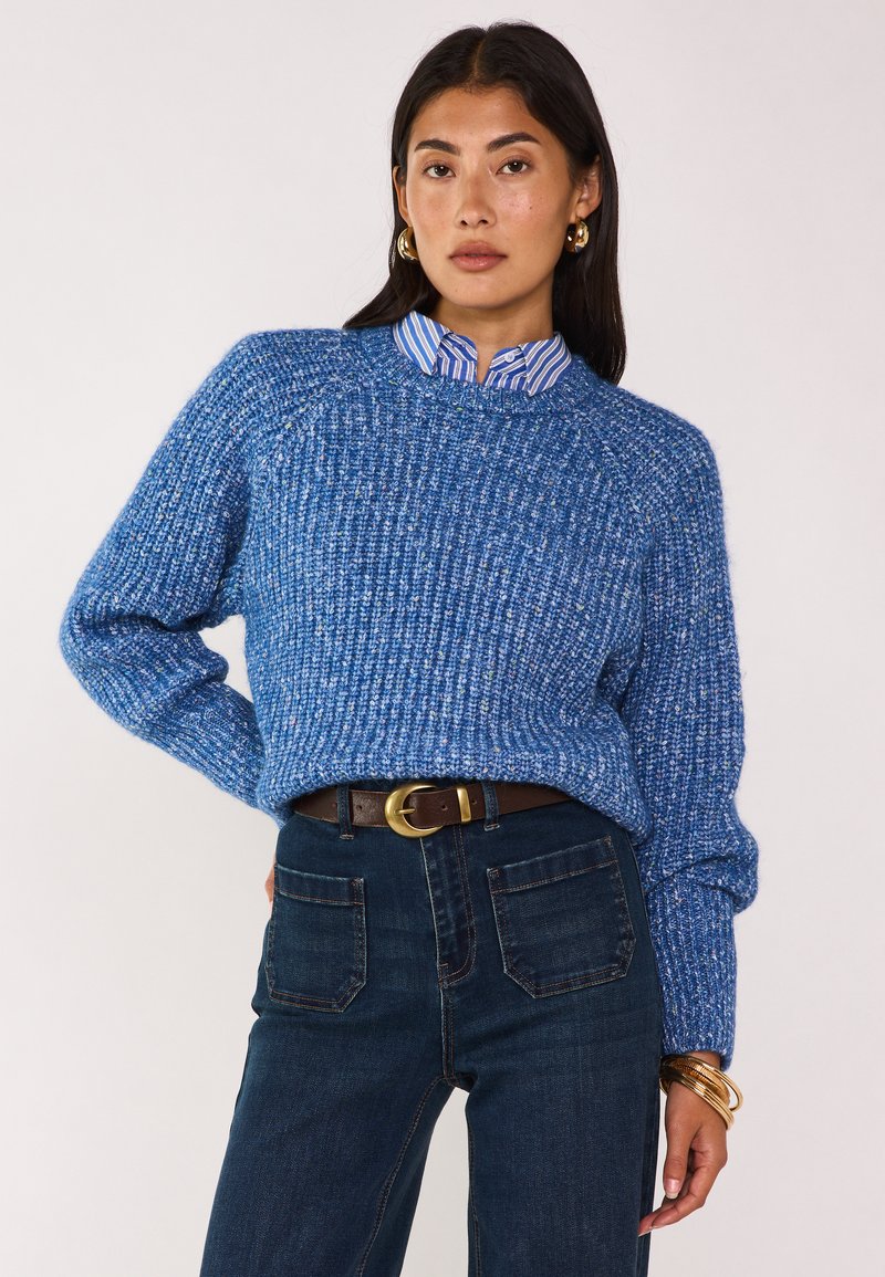 Maglione blu lavorato a maglia con un motivo testurizzato, abbinato a una camicia a righe con colletto e jeans in denim scuro, accentuato da una cintura marrone.