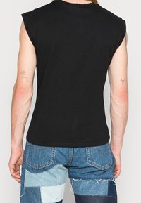 Czarna, bezrękawnikowa koszulka o luźnym kroju, wykonana z miękkiego materiału, z okrągłym dekoltem. Noszona z dżinsami z wielokolorowym patchworkiem.