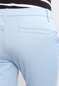 Ljust blå byxor med en jämn textur, som har en enda bakficka och en skräddarsydd passform. Kontrastsydda sömmar synliga längs sömmarna.