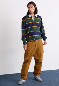 Long-sleeve rugby shirt with green, navy, and orange stripes; white collar. Paired with tan cargo pants and gray athletic shoes.