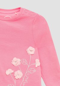 Różowa dziecięca koszulka z długim rękawem, ozdobiona kwiecistymi aplikacjami oraz srebrnymi haftowanymi liśćmi i łodygami, z dwoma zatrzaskami na ramieniu.