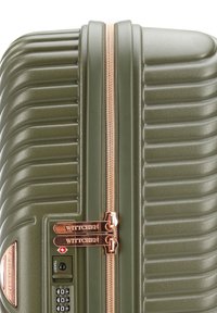 Valise rigide verte avec texture à rayures verticales, fermeture éclair rose doré et tirettes de fermeture éclair doubles étiquetées "WITTCHEN". Équipée d'un cadenas à combinaison.