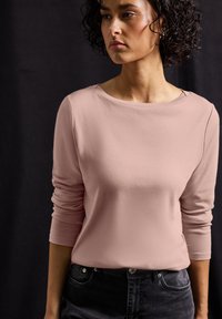 Hellrosa Langarmoberteil mit rundem Halsausschnitt, aus weichem Material. Kombiniert mit dunklen Jeans, die eine glatte Textur und ein einfaches Design zeigen.